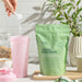 Green package of creatine monohydrate with a pink cup and spoon on a kitchen counter.