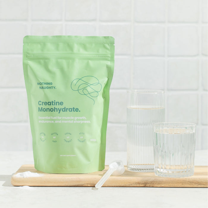 Green package of creatine monohydrate on a wooden board with glasses of water.