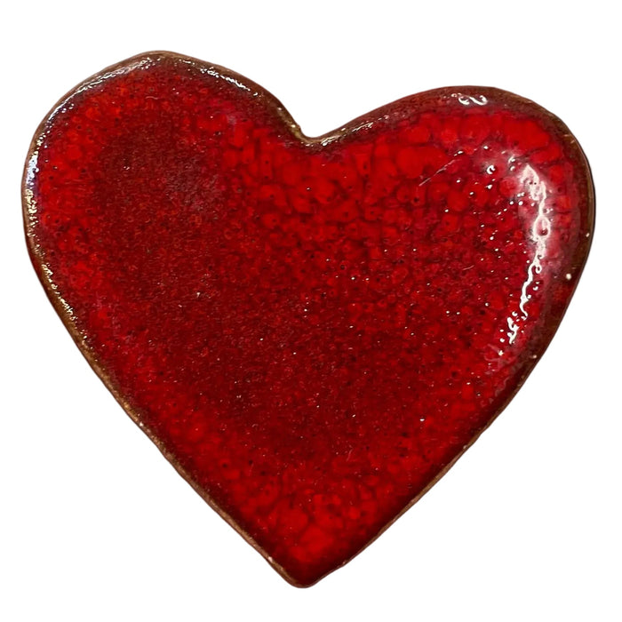 Red heart-shaped object held in a hand against a gray concrete background